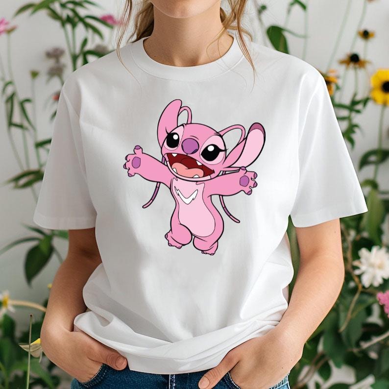 May include: White t-shirt with a pink cartoon character design. The character has large eyes, open arms, and a wide smile. The character has large ears and a light pink color scheme. The shirt is made of a soft material.