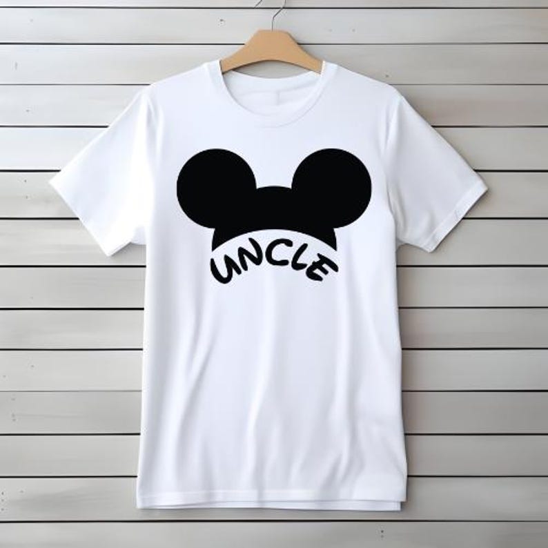 May include: White t-shirt with a black graphic of Mickey Mouse ears and the word "UNCLE" in a curved font. The shirt is hanging on a wooden hanger against a white and gray wood-paneled wall.