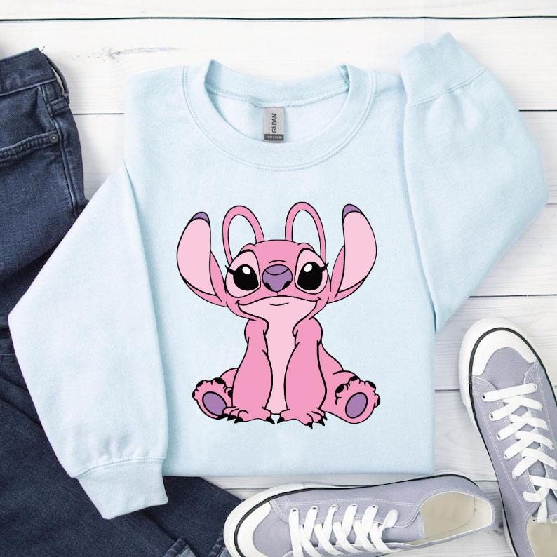 May include: A pale blue sweatshirt with a pink cartoon character design. The character has large ears and is sitting down. The sweatshirt is shown with blue jeans and grey trainers.