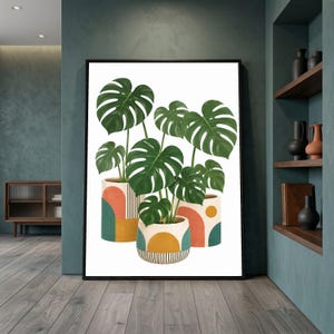 Puede incluir: Una impresión de arte mural enmarcada que muestra tres plantas monstera en macetas con grandes hojas divididas de color verde oscuro. Las macetas son blancas con patrones geométricos en tonos naranja terracota, verde azulado, amarillo mostaza y rayas negras.