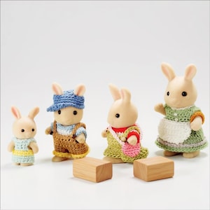 Pode incluir: Quatro figuras de coelhos antropom&oacute;rficos com pelo flocado, vestidas com roupas coloridas de croch&ecirc;. A menor usa um vestido azul e amarelo, a seguinte um bon&eacute; azul e jardineiras castanhas, a terceira um vestido verde com uma bolsa rosa e a maior um vestido verde com um avental branco.