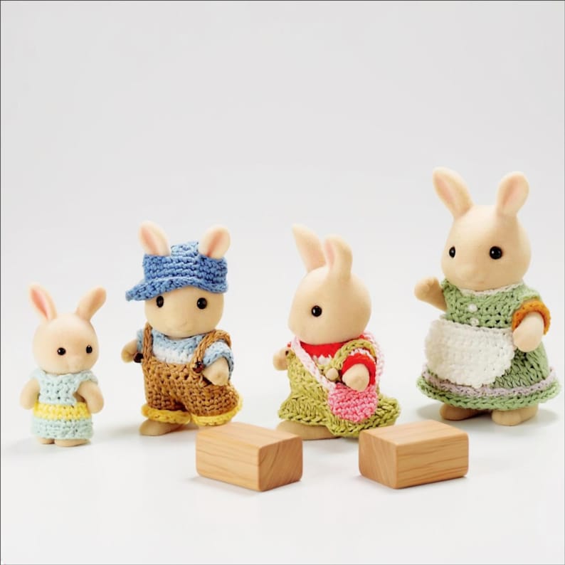Pode incluir: Quatro figuras de coelhos antropom&oacute;rficos com pelo flocado, vestidas com roupas coloridas de croch&ecirc;. A menor usa um vestido azul e amarelo, a seguinte um bon&eacute; azul e jardineiras castanhas, a terceira um vestido verde com uma bolsa rosa e a maior um vestido verde com um avental branco.