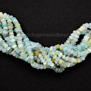 May include: Strands of small, rounded beads in shades of pale blue, green, and yellow. The beads are strung together, forming a necklace or bracelet component. The background is black, highlighting the colors of the beads.
