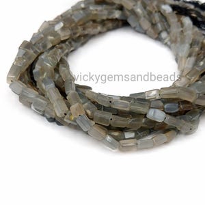 Puede incluir: Cadenas de cuentas rectangulares grises con una apariencia ligeramente translúcida. Las cuentas están ensartadas, formando una forma circular. Las cuentas son de color neutro, adecuadas para la fabricación de joyas.