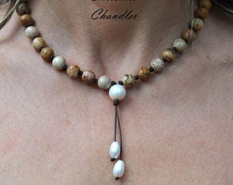 Puede incluir: Un collar de piedras marrones y beige con un colgante de perla blanca y dos perlas más pequeñas que cuelgan del colgante. El collar está en el cuello de una persona y el texto "Christine Chandler" es visible sobre el collar.