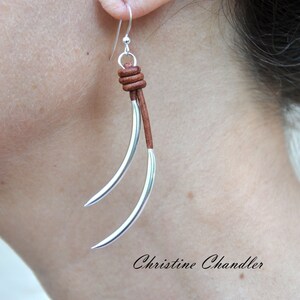 May include: Silver earrings with a brown leather cord and a knot at the top. The earrings are long and dangle.