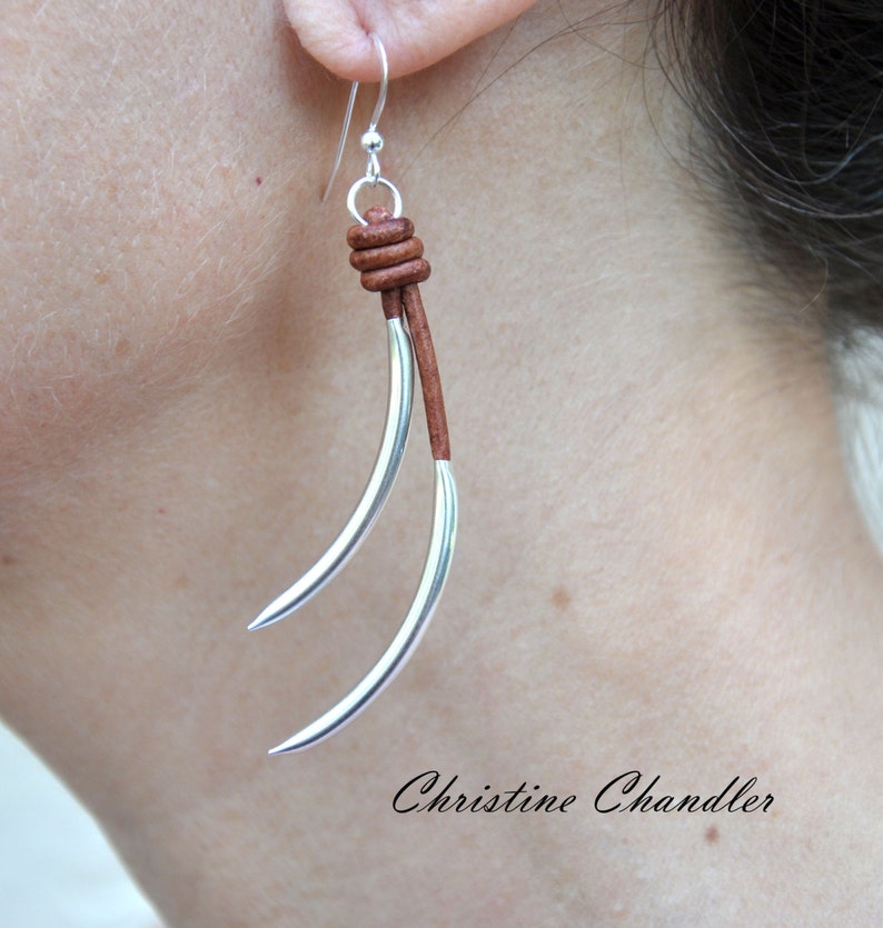 May include: Silver earrings with a brown leather cord and a knot at the top. The earrings are long and dangle.