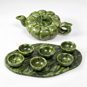 May include: A dark green mottled stone tea set consisting of a pumpkin-shaped teapot with a matching lid, five small round tea cups, and a large oval serving tray. The entire set features a polished finish with natural veining throughout the stone.