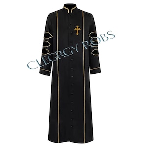 May include: Black clergy robe with gold trim and a gold cross emblem. The robe features a mandarin collar, long sleeves, and decorative cutouts on the upper sleeves. The robe is buttoned down the front and has gold trim along the edges.