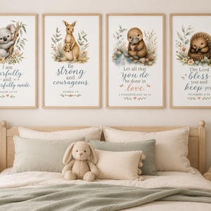 May include: Four rectangular wall art prints in light wood frames featuring watercolour illustrations of a koala, a kangaroo with a joey, a platypus, and a hedgehog, each accompanied by floral accents and inspirational religious text in blue and brown.