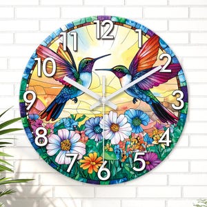Puede incluir: Reloj de pared redondo con diseño de vidriera que representa dos colibríes. La esfera del reloj muestra números y manecillas blancos grandes. Las aves tienen alas coloridas y están sobre un fondo floral con vibrantes tonos azules, naranjas y morados.