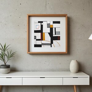 Puede incluir: Impresión artística abstracta en un marco de madera natural. La obra presenta un diseño geométrico con formas negras, blancas, amarillas y rojas. Un pequeño cuadrado azul está en la esquina superior izquierda. La impresión se muestra en una cómoda blanca contra una pared de hormigón gris.