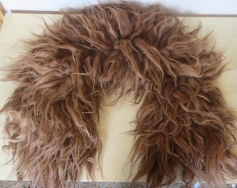 May include: A brown, shaggy faux fur collar. The collar is a U-shape, with long, textured strands of fur. The fur is a mix of light and dark brown tones, creating a natural look. The collar is likely for a costume or fashion accessory.