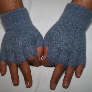 Puede incluir: Un par de guantes azules sin dedos con un patrón texturizado. Los guantes están hechos de un material de punto suave y tienen aberturas para los dedos. Los guantes están diseñados para mantener las manos calientes y permitir la destreza.