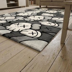 May include: A rectangular area rug featuring a repeating pattern of stylized cartoon skulls with cross-shaped eyes. The design utilizes a monochromatic color palette of white, light gray, dark gray, and black, creating a bold graphic aesthetic.