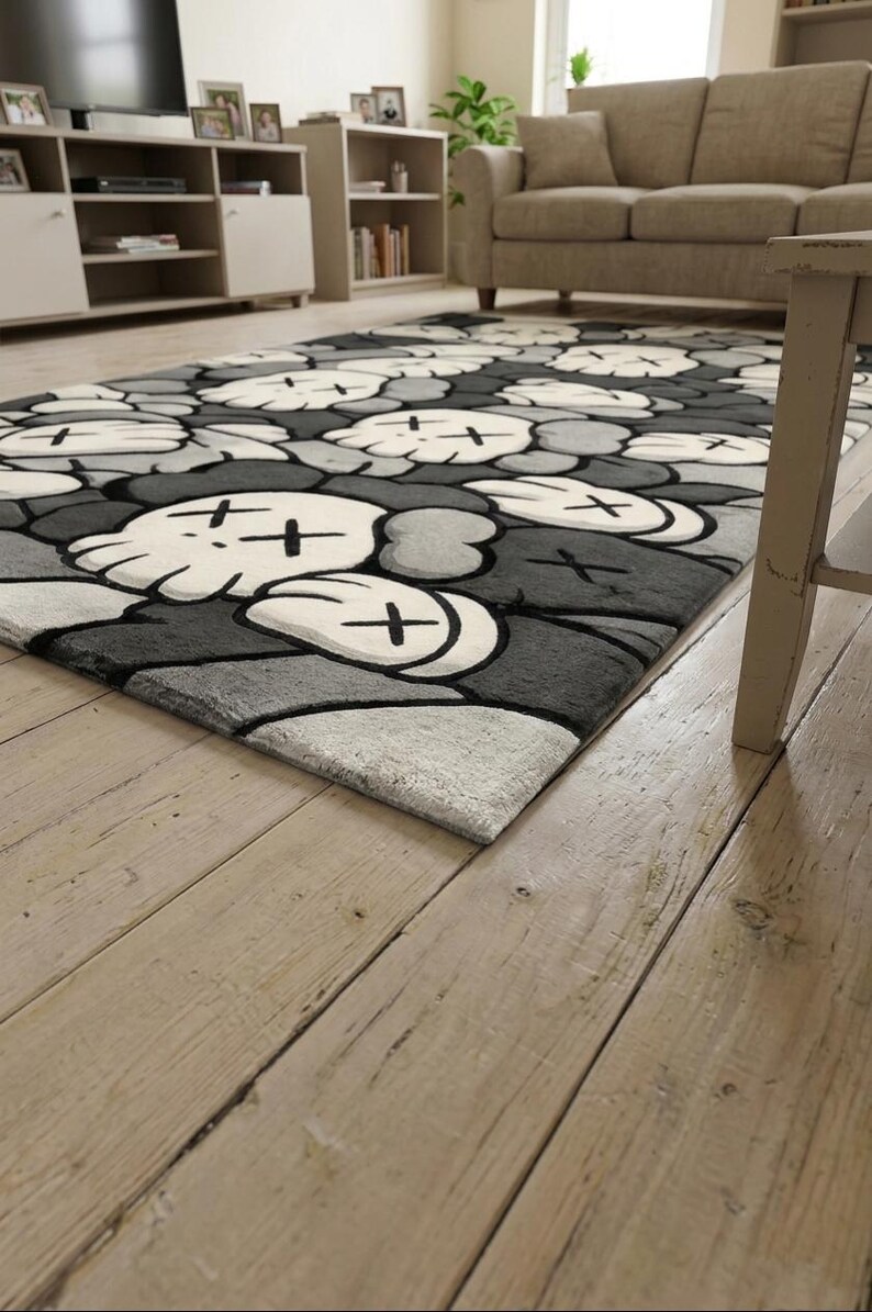 May include: A rectangular area rug featuring a repeating pattern of stylized cartoon skulls with cross-shaped eyes. The design utilizes a monochromatic color palette of white, light gray, dark gray, and black, creating a bold graphic aesthetic.