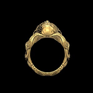 May include: A gold ring with an ornate design. The ring features a detailed, sculpted design with a central, rounded element and intricate patterns along the band. The ring is set against a black background, highlighting its golden color and craftsmanship.