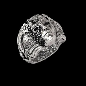 May include: A silver ring featuring a detailed mask design. The ring showcases a half-mask with intricate patterns, a floral element, and a sculpted face. The ring's design is highly detailed, with a polished finish.