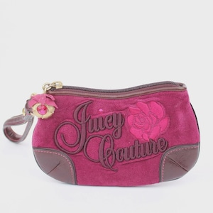 May include: A magenta Juicy Couture clutch bag with a rose applique and the brand name embroidered on the front. The bag has a brown zip and trim, a wrist strap, and a charm with a pink gem.