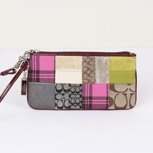 May include: A rectangular wristlet featuring a patchwork design of pink plaid, beige suede, brown signature logo canvas, metallic silver, and lime green panels. It has a dark red leather trim, a zipper closure, and a matching wrist strap with a Coach tag.