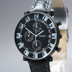 May include: A black Seiko chronograph watch with a black dial, white Arabic numerals, and three sub-dials. The watch features a tachymeter scale on the outer rim, white hands, and a black leather strap with visible white stitching and a metal buckle.