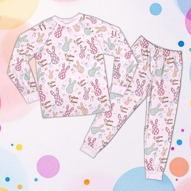 May include: A white pajama set with a repeating pattern of pastel-coloured bunnies and bows. The long-sleeved top and pants feature the text "Custom Name". The pajamas are made of a soft material.