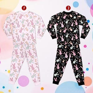 May include: Two sets of pyjamas. One set is white with a pattern of pink, green, and blue bunnies, guitars, and musical notes. The other set is black with the same pattern. Each pyjama set has the text "Custom Home".