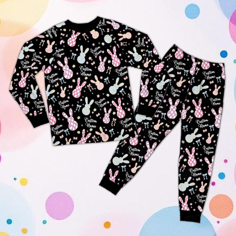 May include: Black pajama set with a repeating pattern of bunny rabbits in pink, blue, and yellow. The long-sleeved top and pants feature the text "Custom Name". The pajamas have black cuffs and a black crew neck.