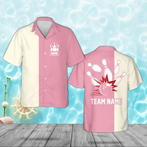 Peut inclure: Chemise de bowling à manches courtes avec un design divisé. Un côté est crème, l'autre rose. L'avant présente un graphisme de quilles et le mot "NAME". Le dos a un graphisme de boule et de quilles avec "TEAM NAME".