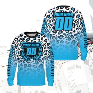 May include: Long-sleeved jersey with a blue and white leopard print design. The jersey features a shield with the text "YOUR NAME" and the numbers "00" in blue. The sleeves have the text "CUSTOM TEXT" in blue.