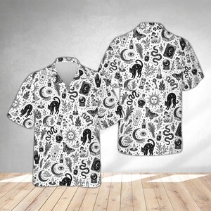 May include: A short-sleeve button-down shirt featuring an all-over black and white print of mystical symbols including cats, crescent moons, suns, snakes, moths, crystal balls, candles, potion bottles, and hands with eye motifs on a white background.