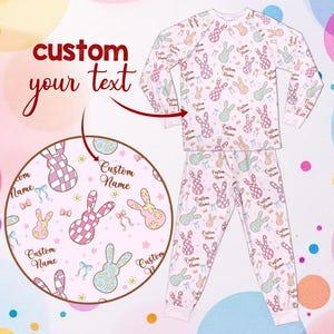 May include: A light pink pajama set featuring a pattern of pastel bunnies, bows, and the text "Custom Name." The long-sleeved top and trousers are designed for comfort. The words "custom your text" are in the upper left corner.