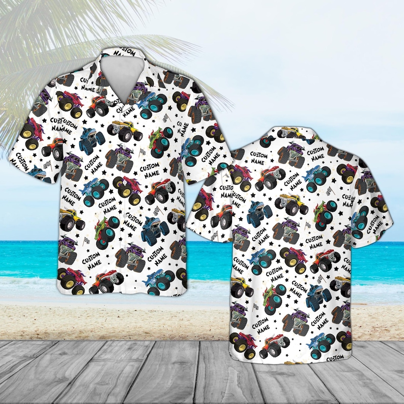 May include: White short-sleeve button-down shirt featuring a repeating pattern of colorful monster trucks, stars, and checkered flags. The text "CUSTOM NAME" is also printed on the shirt. The shirt is displayed on a wooden surface with a beach and ocean background.