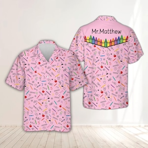 Può includere: Una camicia a maniche corte con bottoni in rosa chiaro con un motivo ripetuto di pastelli colorati, mele, equazioni matematiche e la parola Teacher. Il retro mostra una fila di pastelli e il testo Mr.Matthew in caratteri neri.