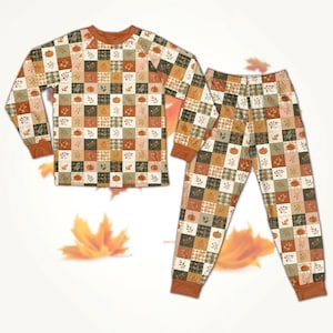 May include: A long-sleeved top and trousers pyjama set featuring a patchwork grid pattern. Each square contains illustrations of pumpkins, autumn leaves, or plaid textures in shades of orange, brown, cream, and dark green with solid cuffs.