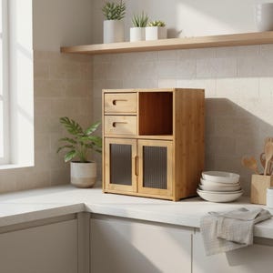 May include: A light brown bamboo kitchen cabinet with two drawers, a central open shelf, and two glass-paned doors. The cabinet is on a white countertop, with plants and dishes nearby. The cabinet is a storage solution for the kitchen.