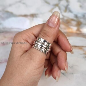 May include: A silver ring with a hammered texture and a spinning design. The ring is worn on a finger, showcasing its multiple bands and polished finish. The ring is a piece of jewelry.