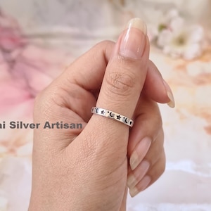 May include: A silver ring with a celestial design featuring cut-out stars and crescent moons. The ring is worn on a finger, showcasing the intricate details of the jewelry. The text "Sai Silver Artisan" is visible in the image.