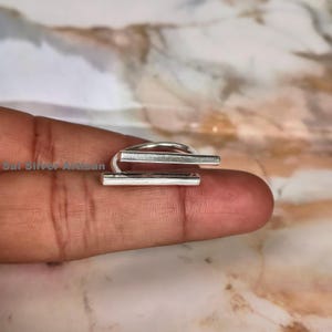 May include: A silver ring with a modern design. The ring features two parallel rectangular bars connected by a curved band. The ring is shown on a finger.