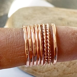 Könnte beinhalten: Eine Sammlung von roségoldenen Ringen in verschiedenen Ausführungen, darunter gehämmert und gedreht. Die Ringe sind auf einem Finger gestapelt und zeigen ihre unterschiedlichen Texturen und Oberflächen. Die Ringe haben eine warme, metallische Farbe.