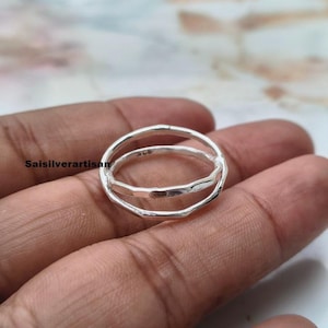 May include: A silver ring featuring a double band design with a hammered, textured finish. The metal surface reflects light, showing a bright, polished appearance. The text Saisilverartisan is visible on the left side of the image background.