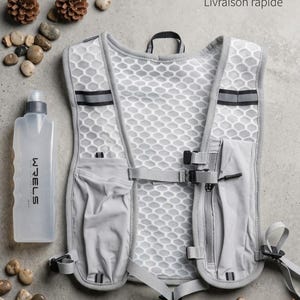 Può includere: Un gilet da corsa grigio con una borraccia da 350 ml. Il gilet presenta un design a rete a nido d'ape e diverse tasche. La borraccia è trasparente con il marchio "WRELS" stampato sopra. Il testo "Gilet de course + gourde 350ml" è visibile.