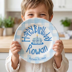 Może przedstawiać: Biały ceramiczny talerz z niebieskim obramowaniem w kratkę. Talerz zawiera napis "Happy Birthday Rowan" w kolorze niebieskim, ilustrację tortu i datę "4 września 2025 r.".