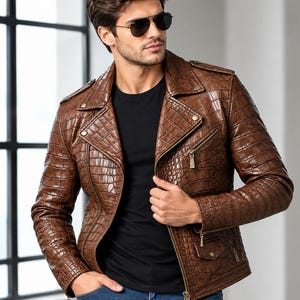 Könnte beinhalten: Eine braune Lederjacke mit texturiertem Krokodilleder-Muster, ausgestattet mit einem fallenden Revers, silberfarbenen Metallreißverschlüssen an Brust und Ärmelbündchen, Druckknopfdetails an den Schultern und einem Frontreißverschluss über einem schwarzen T-Shirt.