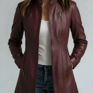 May include: A long-length burgundy leather jacket featuring a stand-up collar with a snap button closure, a full-length front zipper, and four vertical zippered pockets on the front. The jacket is worn over a white tank top and blue denim jeans.