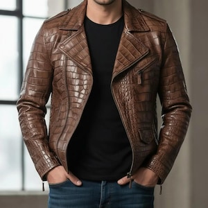 Może przedstawiać: Brązowa skórzana kurtka z fakturą imitującą skórę krokodyla. Kurtka posiada kołnierz z klapami, zapięcie na zamek błyskawiczny i kilka kieszeni. Osoba ma na sobie czarny t-shirt i niebieskie dżinsy.