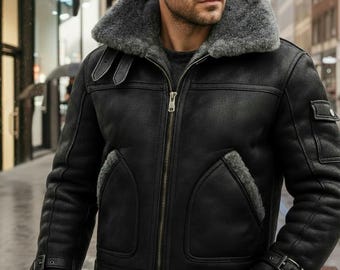 May include: A black jacket with a thick grey shearling lining and collar. The jacket features a front zipper closure, two side pockets, and adjustable buckle straps on the cuffs and near the collar. A small pocket is visible on the upper left sleeve.