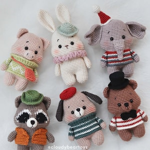 Puede incluir: Seis animales de peluche tejidos a ganchillo que incluyen un cerdo con suéter verde, un conejo con sombrero verde y bufanda rosa, un elefante con suéter a rayas y gorro rojo, un mapache con sombrero verde y chaleco naranja, un perro con boina roja y un oso con sombrero de copa.