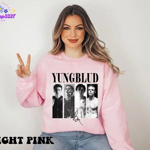May include: Light pink sweatshirt featuring the band name "YUNGBLUD" in bold black letters above four black and white images of the band members. The sweatshirt also has the words "LIGHT PINK" in black at the bottom.