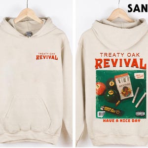 May include: Sand-coloured hoodie with the text "TREATY OAK REVIVAL" in red on the front and back. The back features a graphic with pool balls, a cigarette pack, and the phrase "HAVE A NICE DAY".